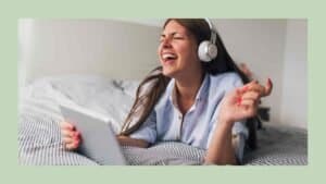 Singer in a rust-colored sweater with curly brown hair, eyes closed, singing into a black microphone while her hand rests on her chest and a music stand is blurred behind her.
